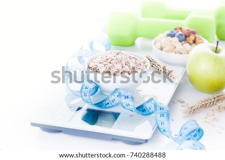 Electronic digital kitchen scale with oatmeal, apple, measuring tape and green dumbbells on background