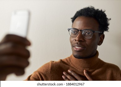 Electronic gadgets, distant socializing and connection. Fashionable dark skinned guy with bristle reaching out hand holding mobile phone chatting online using video call app, taking to mother