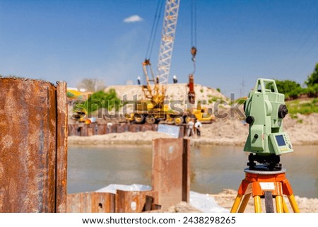 Electronic leveler device ensure precise measurements before undertaking large construction projects. Metal piles for bridge foundation along coast, across river is mobile crane    