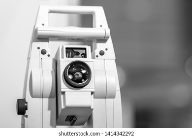 Electronic optical measuring device in white. Has the lens and viewfinder. The background is gray and blurred.