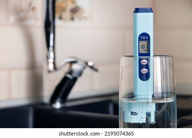 Electronic PH Meter In A Glass Of Water. In The Background There Is A Tap For Drinking Water. The Concept Of Testing Water For Miralization. Water Test