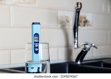 Electronic PH Meter In A Glass Of Water. In The Background There Is A Tap For Drinking Water. The Concept Of Testing Water For Miralization. Water Test