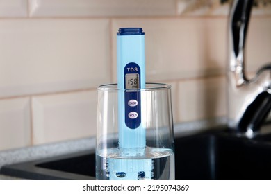 Electronic PH Meter In A Glass Of Water. In The Background There Is A Tap For Drinking Water. The Concept Of Testing Water For Miralization. Water Test