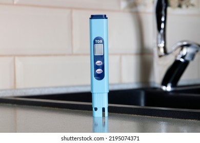 Electronic PH Meter In A Glass Of Water. In The Background There Is A Tap For Drinking Water. The Concept Of Testing Water For Miralization. Water Test