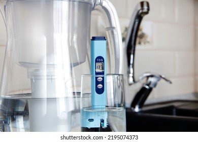 Electronic PH Meter In A Glass Of Water. In The Background There Is A Tap For Drinking Water. The Concept Of Testing Water For Miralization. Water Test