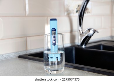 Electronic PH Meter In A Glass Of Water. In The Background There Is A Tap For Drinking Water. The Concept Of Testing Water For Miralization. Water Test