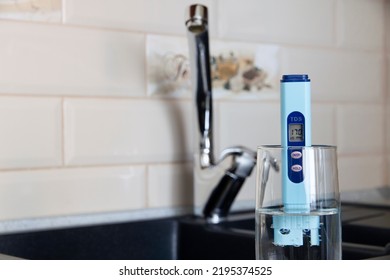 Electronic PH Meter In A Glass Of Water. In The Background There Is A Tap For Drinking Water. The Concept Of Testing Water For Miralization. Water Test