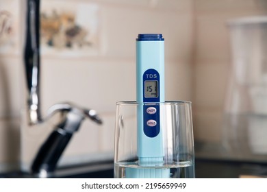 Electronic PH Meter In A Glass Of Water. In The Background There Is A Tap For Drinking Water. The Concept Of Testing Water For Miralization. Water Test