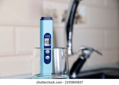 Electronic PH Meter In A Glass Of Water. In The Background There Is A Tap For Drinking Water. The Concept Of Testing Water For Miralization. Water Test