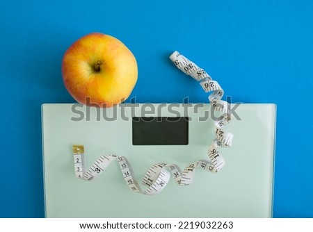 Electronic scales, centimeter tape and an apple on a blue background, photo.