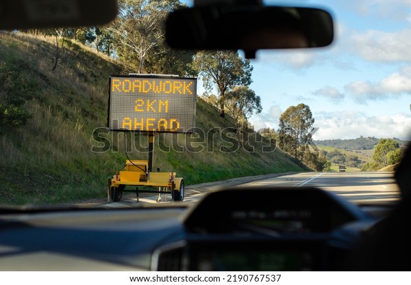 Electronic screen road sign\
with text \
\'roadwork 2km ahead\' on side of an Australian country\
highway.
