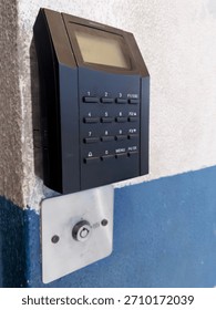 Electronic security access control keypad and reader mounted on a white and blue wall. A modern digital punch clock system for office entry and attendance.
