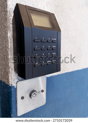 Electronic security access control keypad and reader mounted on a white and blue wall. A modern digital punch clock system for office entry and attendance.