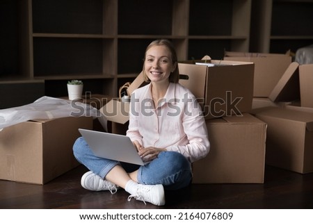 Electronic services buyer, make order, user of remotely retail e-services, happy homeowner buy goods, furniture for new flat via webstore. Young woman sit on floor with laptop near boxes on moving day