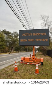 Electronic Sign Near A Road That Says, Active Shooter Take Cover Now. There Is A Blue Sky And Cars On The Highway