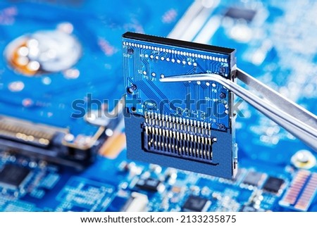 Electronic technician holding tweezers with microchip and assemblin a circuit board. Production computer or repair pc system. Selective focus.
