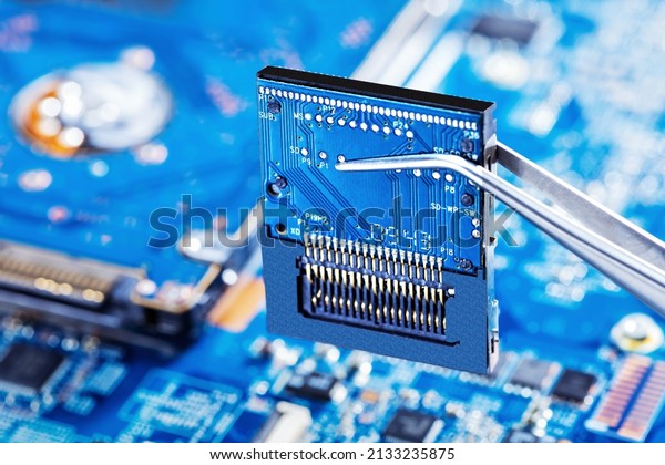 Electronic technician holding tweezers with\
microchip and assemblin a circuit board. Production computer or\
repair pc system. Selective\
focus.