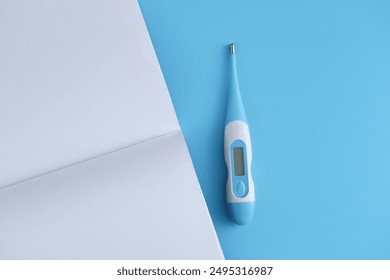 Electronic thermometer with a blank open notebook on a blue background. Medicine concept