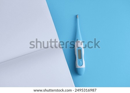 Electronic thermometer with a blank open notebook on a blue background. Medicine concept