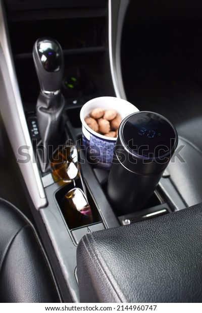 Electronic thermos of\
hot coffee tea, cookies snack in paper glass placed in holder\
inside of car near hand break, automobile, vehicle for drinking,\
eating during long\
drive.