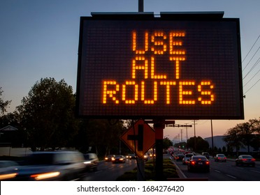 Electronic Traffic Sign Stating Use Alternate Routes With Blurred Traffic