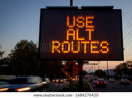 Electronic traffic sign stating Use Alternate Routes with blurred traffic