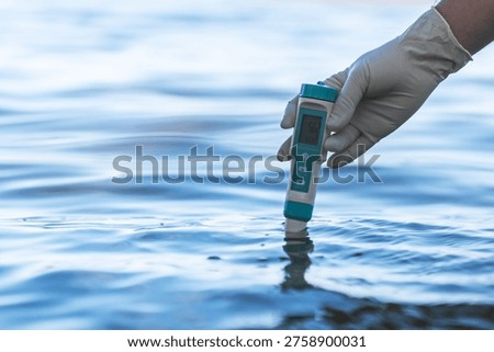 Electronic water testing hand over blurred blue swimming water background, water quality check. testing the level of water pollution in a natural reservoir.