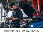 Electronics adjustment, with digital tablet. Mechanic working in a car service station.