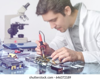 Electronics background. Young energetic male tech or engineer repairs electronic equipment in research facility. Shallow DOF, focus on the hands of the worker. This image is toned. - Powered by Shutterstock