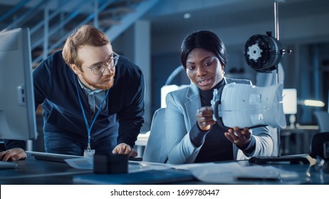 Electronics Development Engineer Working at His Desk, Talks with Project Manager, Shows Mechanism Prototype Construction. Team of Professionals Working in the Modern Technology Designing Agency. - Shutterstock ID 1699780447
