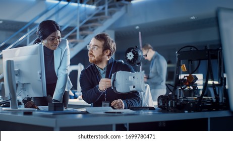 Electronics Development Engineer Working at His Desk, Talks with Project Manager, Shows High Tech Prototype Component. Team of Professionals Working in the Modern Technology Designing Agency. - Powered by Shutterstock