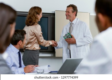Electronics engineer and businesswoman shake hands in conference room