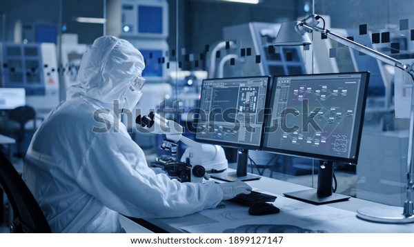 Electronics Factory Cleanroom: Engineer\
Scientist in Coveralls Works on Computer, Screen Shows Infographics\
and Software System Control UI, Developing Electronics for Medical\
Electronics