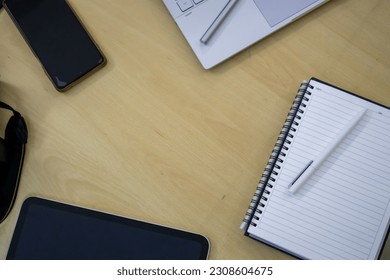 Electronics items on a table along with a notebook, tablet and laptop.
