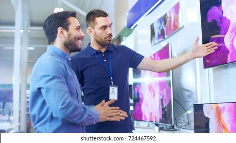 In the Electronics Store Professional Consultant Shows Latest 4K UHD TV's to a Young Man, They Talk about Specifications and What Model is Best for Young Man's Home. Store is Bright. - Powered by Shutterstock