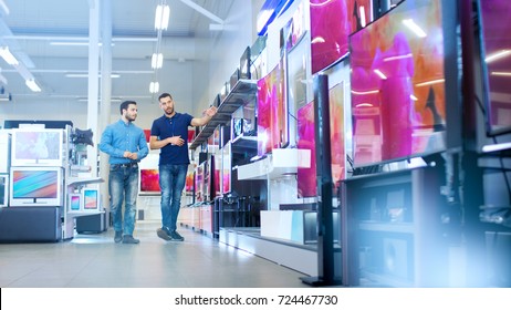 In the Electronics Store Professional Consultant Shows Latest 4K UHD TV's to a Young Man, They Talk about Specifications and What Model is Best for Young Man's Home. Store is Bright. - Shutterstock ID 724467730