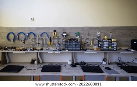 Electronics workstation modular storage units with sorted components, handheld tools hanging on a wooden wall panel, soldering equipment, and multiple laptops arranged on desks for technical repair