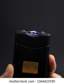 Electroshock Taser In The Hand Of A Man On A Black Background.