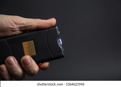 Electroshock Taser In The Hand Of A Man On A Black Background.