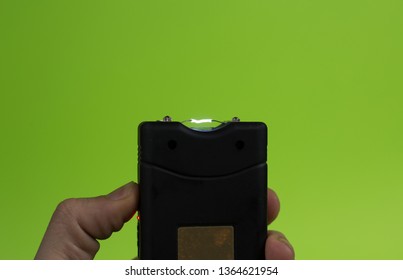 Electroshock Taser In The Hand Of A Man On A Green Background.