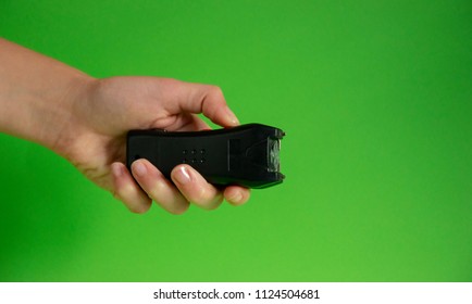 Electroshock Taser In The Hand Of A Woman On A Green Background, Methods Of Self Defense, Danger