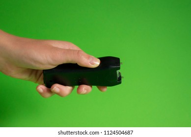 Electroshock Taser In The Hand Of A Woman On A Green Background, Methods Of Self-defense, Danger