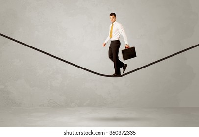 An Elegan Businessman In Suit Balancing On A Tight Rope With A Briefcase In Front Of Grey Urban Wall Background Environment Concept