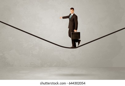 An Elegan Businessman In Suit Balancing On A Tight Rope With A Briefcase In Front Of Grey Urban Wall Background Environment Concept