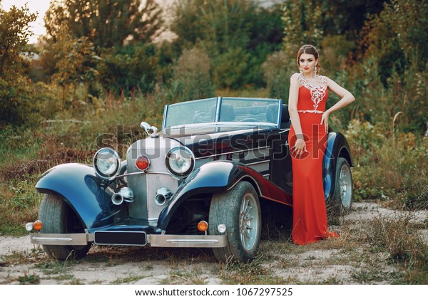 Elegance lady in a red dress standing near a retro\
blue car