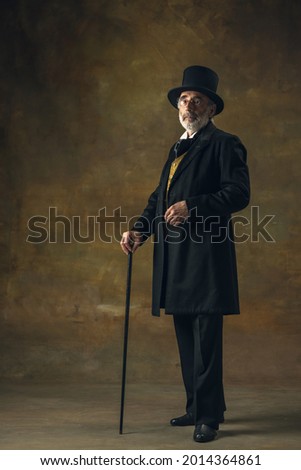 Elegance, loftiness. Portrait of elderly gray-haired man, gentleman or actor posing isolated on dark vintage background. Retro style, comparison of eras concept. Old male model like aristoctar.