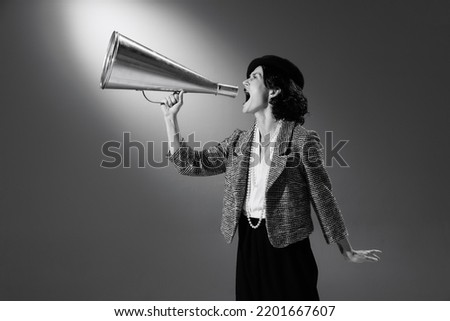 Elegance. Portrait of beautiful woman in stylish classic suit shouting in megaphone. Black and white photography. Big sales. Monochrome effect. Concept of fashion, style, history