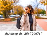 Elegant african american young businesswoman wearing trench coat carrying hand bag in the city in autumn