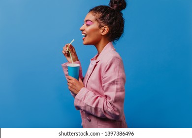 Elegant African Lady Drinking Soda. Adorable Curly Girl In Pink Jacket Standing On Blue Background.