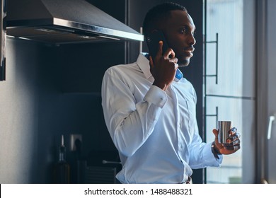 Elegant african man is enjoying his morning coffee while talking by mobile phone at his kitchen. - Powered by Shutterstock